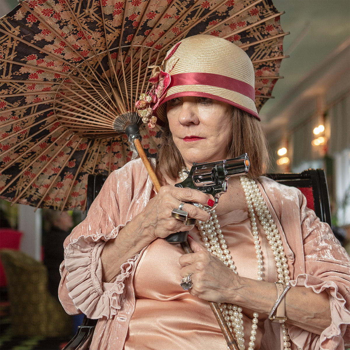 A person in 1920s attire holding a parasol and a gun.